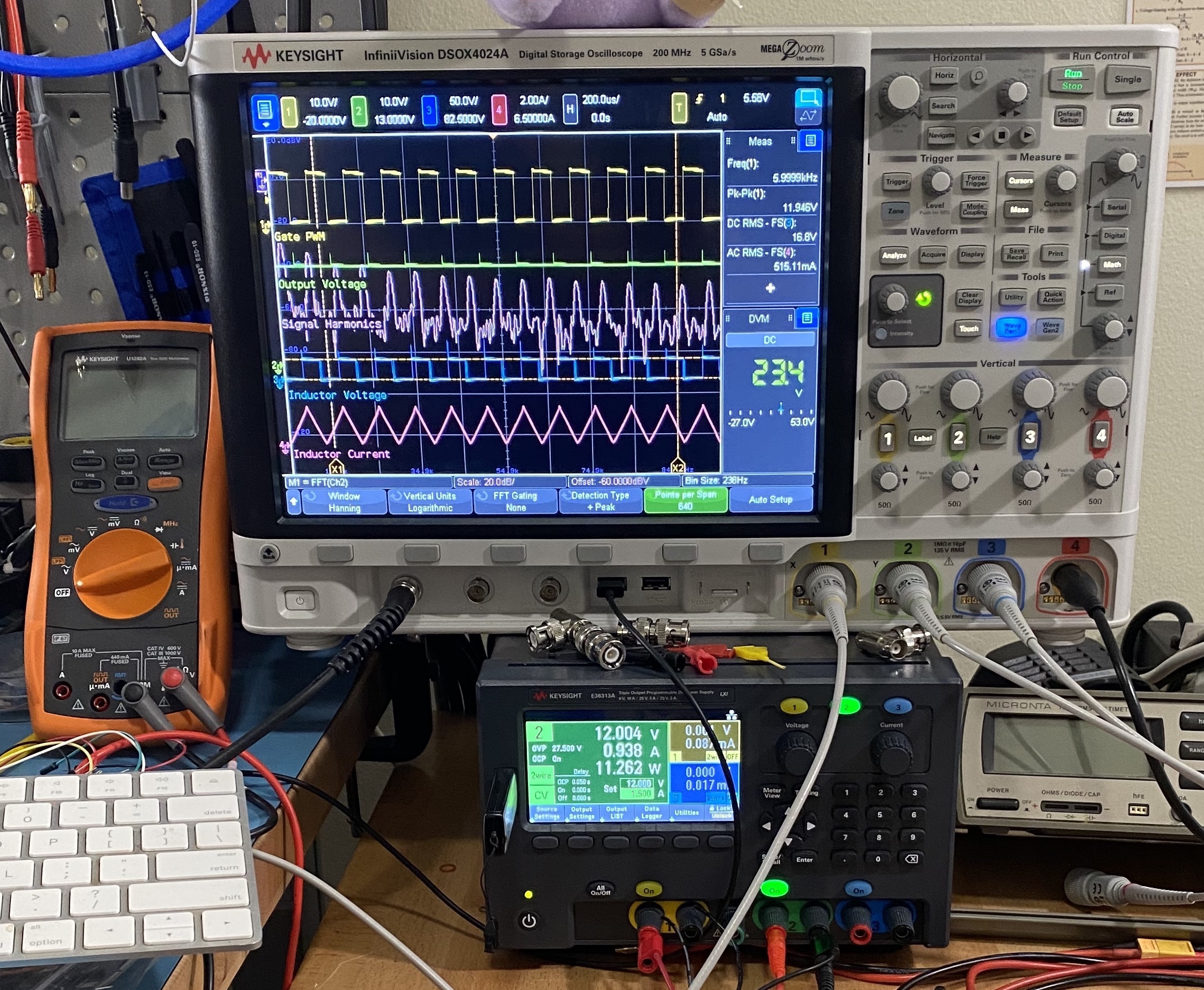 Digital oscilloscope showing waveforms beside a multimeter and bench power supply.